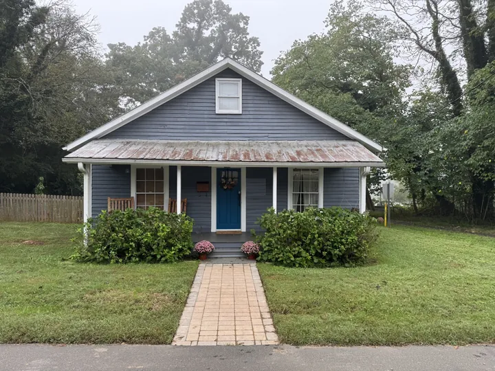 Photo of the real house: a blue clapboard bungalow with a tin porch roof